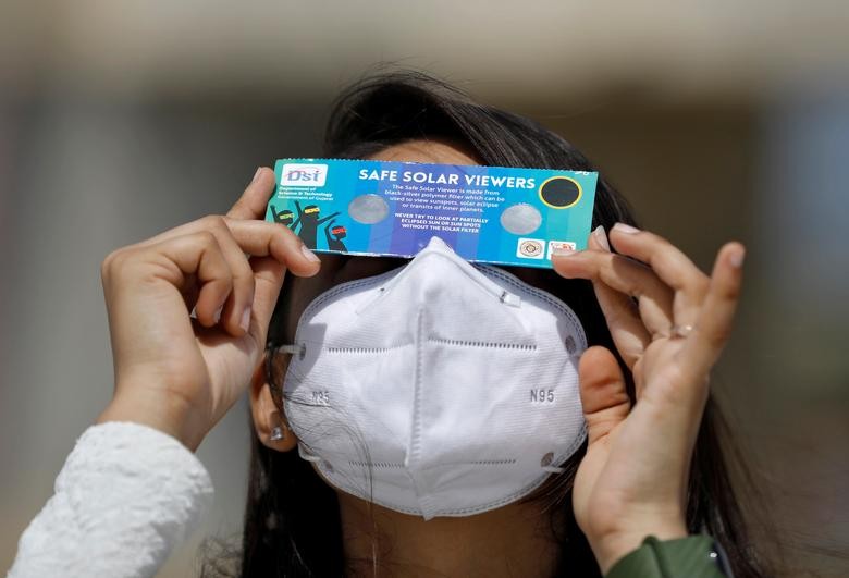A woman, wearing a protective face mask against the coronavirus disease (COVID-19), uses solar viewers to watch a partial solar eclipse at Gandhinagar, India, June 21, 2020. REUTERS/Amit Dave